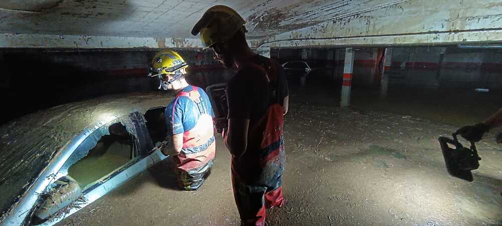 Los bomberos buscando en los coches completamente inundados y llenos de lodo tras sacar el agua de los garajes.